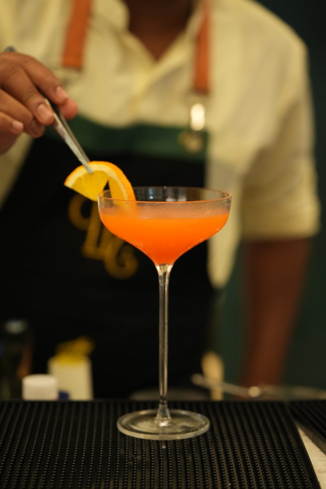 An orange cocktail in a coupe glass, garnished with an orange slice