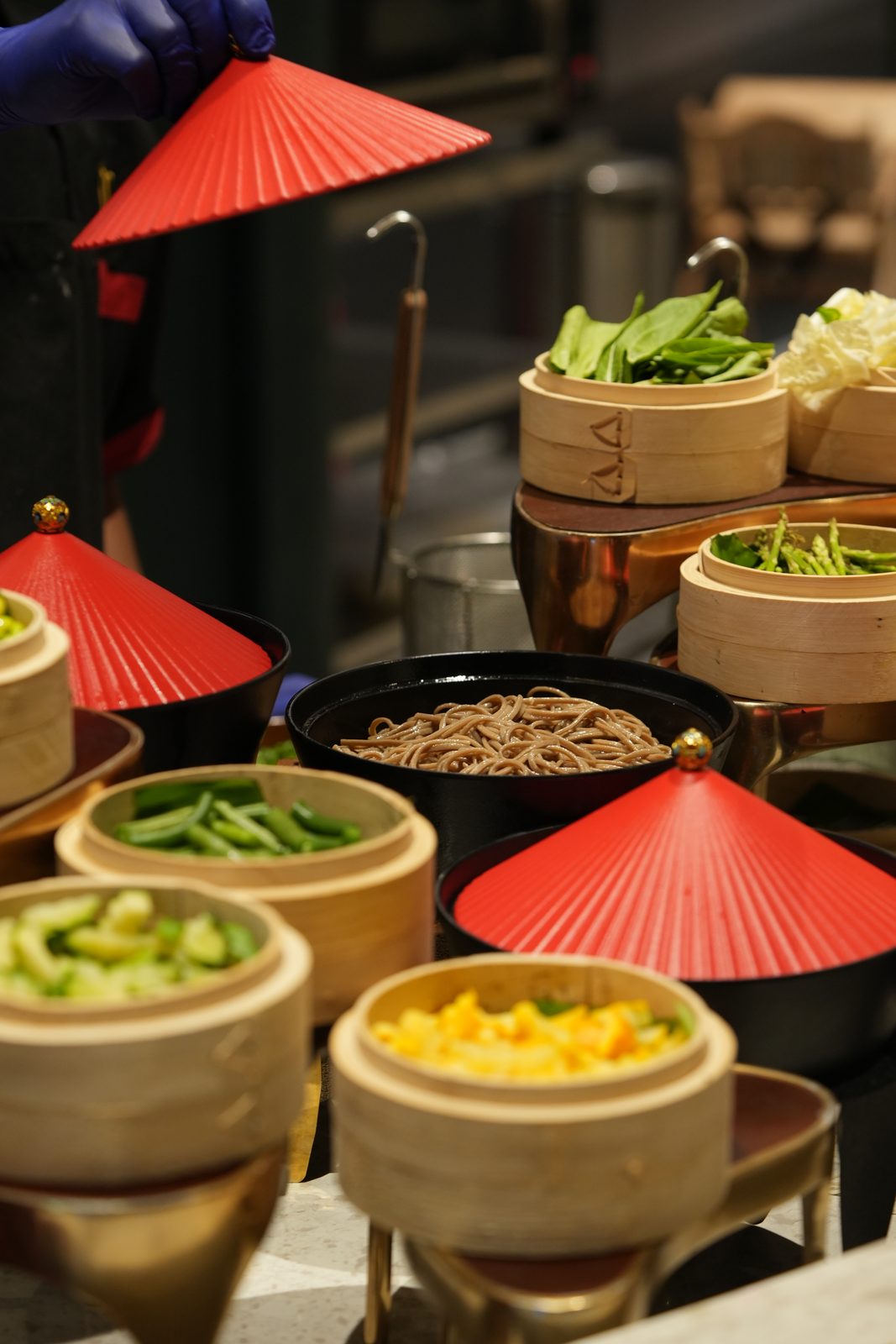 Bamboo steamers of fresh vegetables under red umbrella lids at the wok station