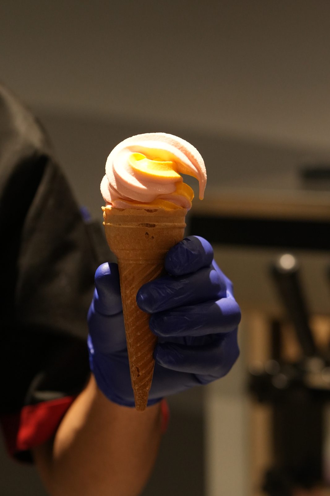 A soft-serve ice cream cone with orange topping held up by a server
