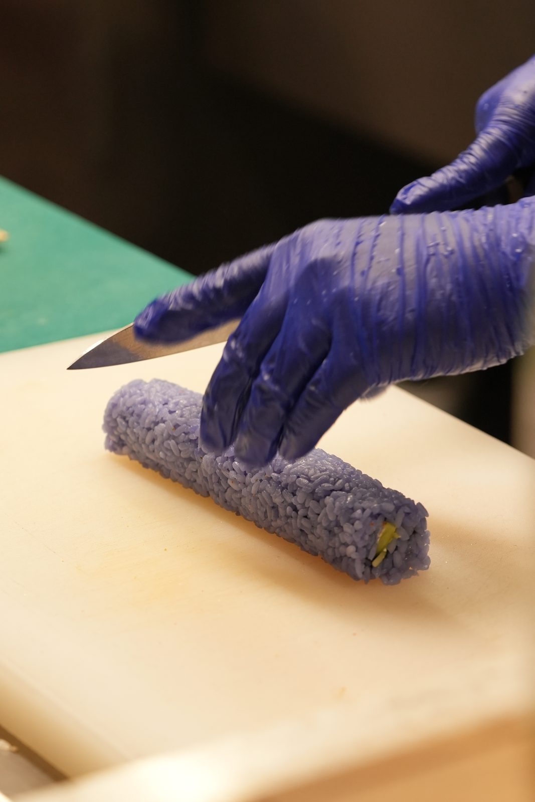 A chef slicing a blue pea sushi roll
