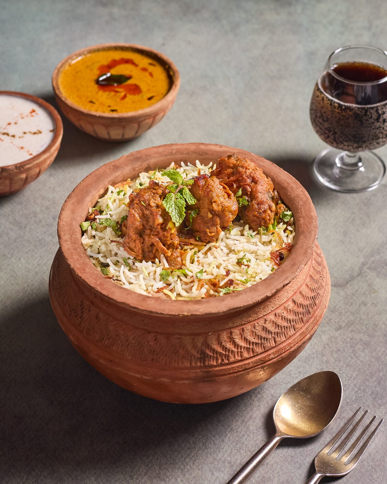Chicken dum biryani in a clay pot with a glass of cola beside it